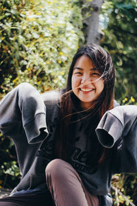 Portrait of smiling young woman sitting against trees