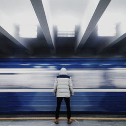 Rear view of man standing against train moving at illuminated subway station