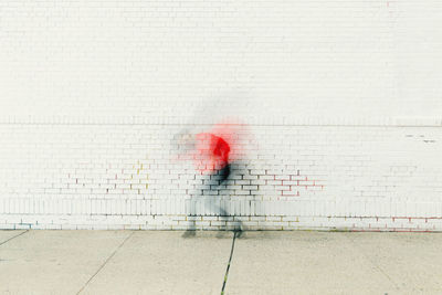 Person walking on footpath against red wall