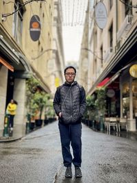 Full length of asian man standing in laneway against buildings in the city.