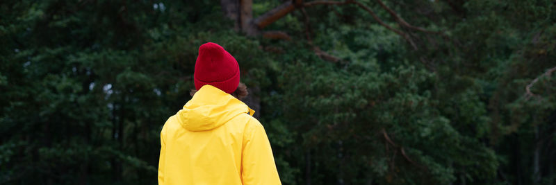 Long width banner with back view of woman in pine forest in bright yellow cloak 