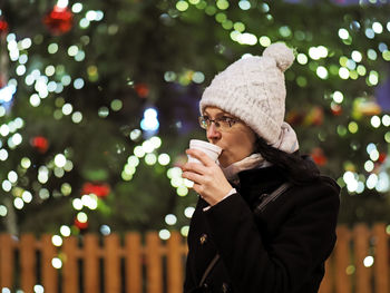 Young woman drinks a hot drink front of a christmas tree