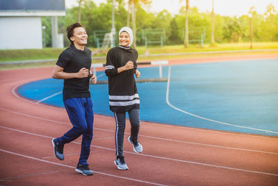 Full length of cheerful couple jogging on running track