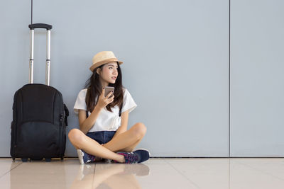 Portrait of young woman sitting on floor against wall