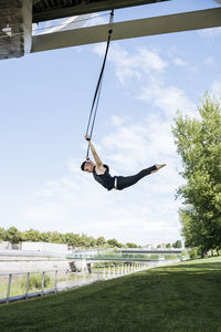 Low angle of fit male gymnast hanging on aerial straps during training in park