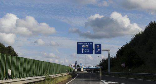 Road sign by trees against sky