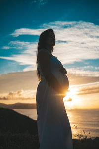 Woman standing at beach against sky during sunset