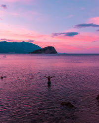 Rear view of shirtless man in sea against sky during sunset