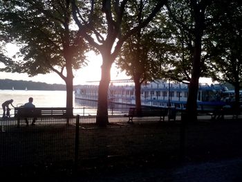 Rear view of woman sitting on railing by river against sky