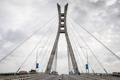 Low angle view of suspension bridge against cloudy sky