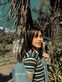 Portrait of smiling young woman standing against tree