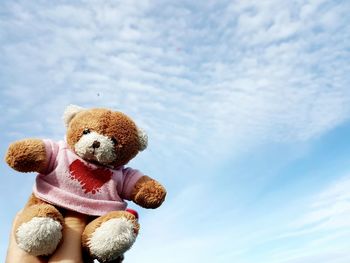 Close-up of hand holding teddy bear against sky