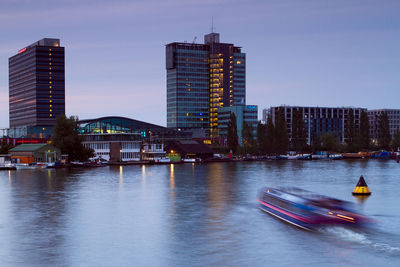 Blurred motion of boat in river by cityscape against sky at dusk