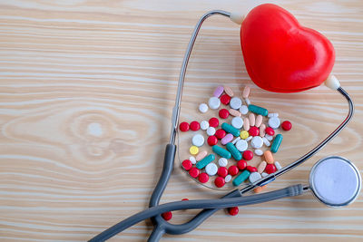 High angle view of multi colored pills with stethoscope and heart shape on table