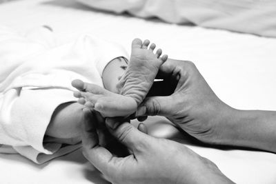 Cropped hands of mother holding baby legs on bed