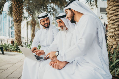 Senior man with grandsons wearing dish dash using laptop outdoors