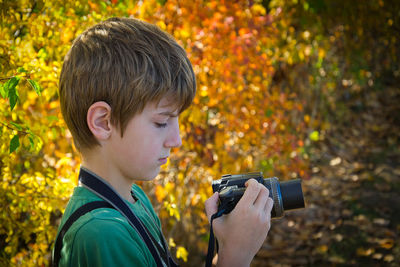 Portrait of boy holding camera during autumn