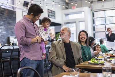 Happy man looking at baby girl being carried by father in restaurant