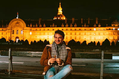 Young man sitting and eating sweets at illuminated city at night