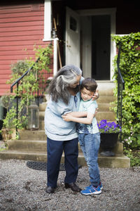 Grandmother embracing grandson in back yard against house