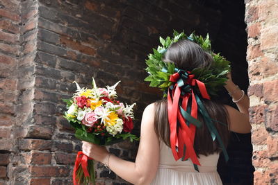 Woman holding flower bouquet against wall