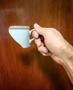 Cropped image of hand holding broken cup against wood