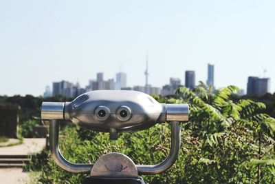 Close-up of coin-operated binoculars against cityscape