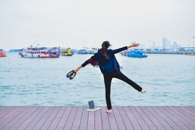 Rear view of woman with arms outstretched standing on pier over sea against sky