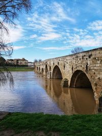 Arch bridge over river against cloudy sky