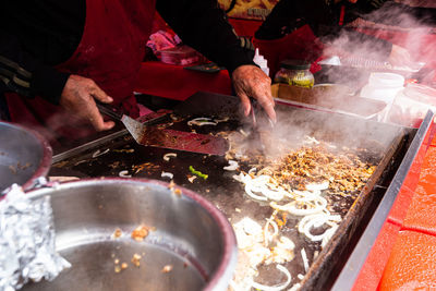 Hands holding cooking utensil spatula cooking food on grill with smoke in food stall at street fair