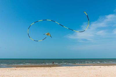 Person flying striped kite at beach against sky