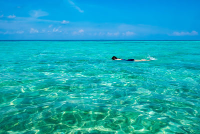 Man swimming in sea against blue sky