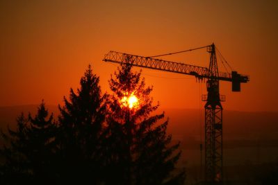 Silhouette trees and crane against sky during sunset