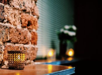 Close-up of illuminated candle in wicker on table by brick wall at hinky dinks