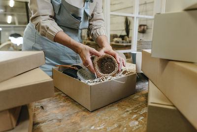 Hands of craftswoman packing crochet decor in box on workbench