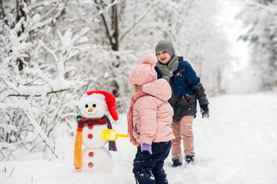 Children making snowman in forest