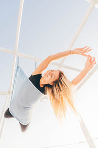 Rear view of woman with arms raised standing against sky