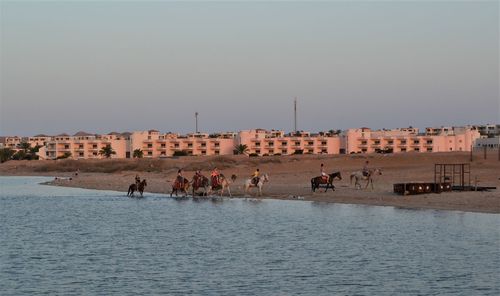 People on beach by buildings against clear sky