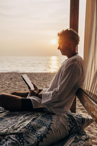Side view of man using tablet pc while sitting in cabana on vacation at beach