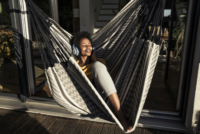 Woman with headphones lying on hammock at balcony