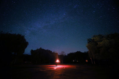 Illuminated street amidst trees against sky at night