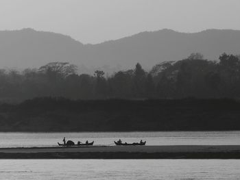 People on lake by mountains against sky