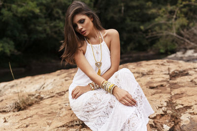 Young woman wearing dress sitting on rock formation at forest
