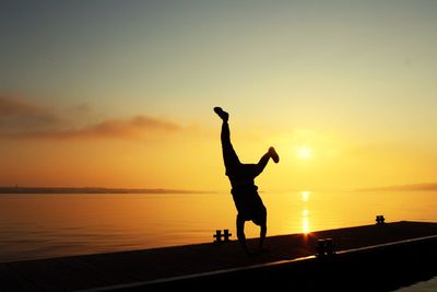 Silhouette man doing handstand on boat in sea during sunset