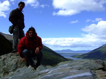 Full length of man sitting on mountain against sky