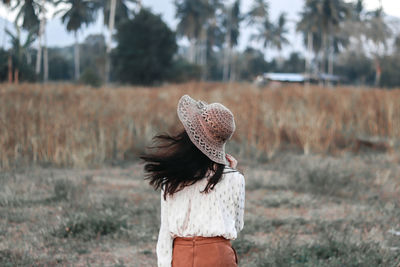 Rear view of woman wearing hat standing on field