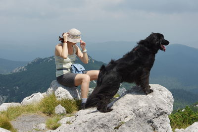 Woman sitting with flat-coated retriever on mountain peak against sky