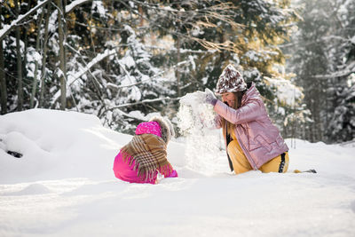 Full length of mother and daughter playing on snow covered land during winter