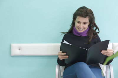 Young woman using mobile phone while sitting on wall