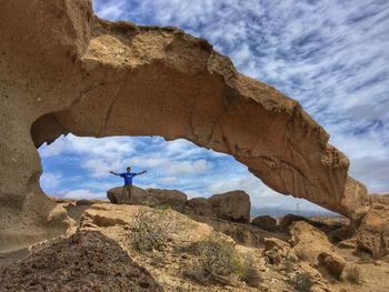 Man standing under rock formation against sky